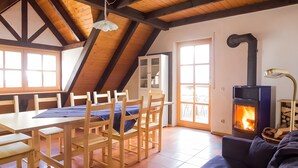 A cozy room with a wooden table, chairs, a sofa, a fireplace, and a window with a view.