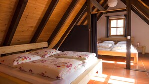 A room with a sloped ceiling, wooden beams, a bed with floral bedding, a window, and a nightstand with a lamp.