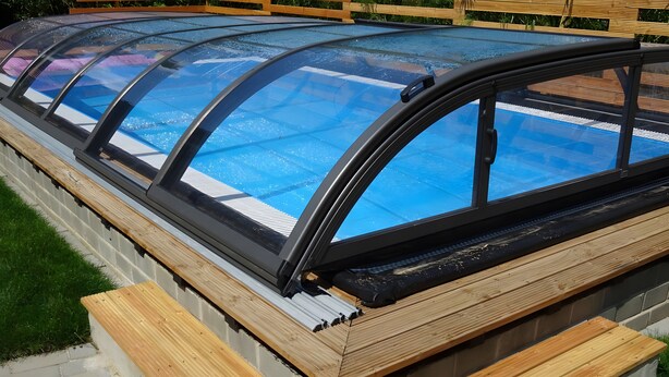 A swimming pool with a glass enclosure and wooden deck.