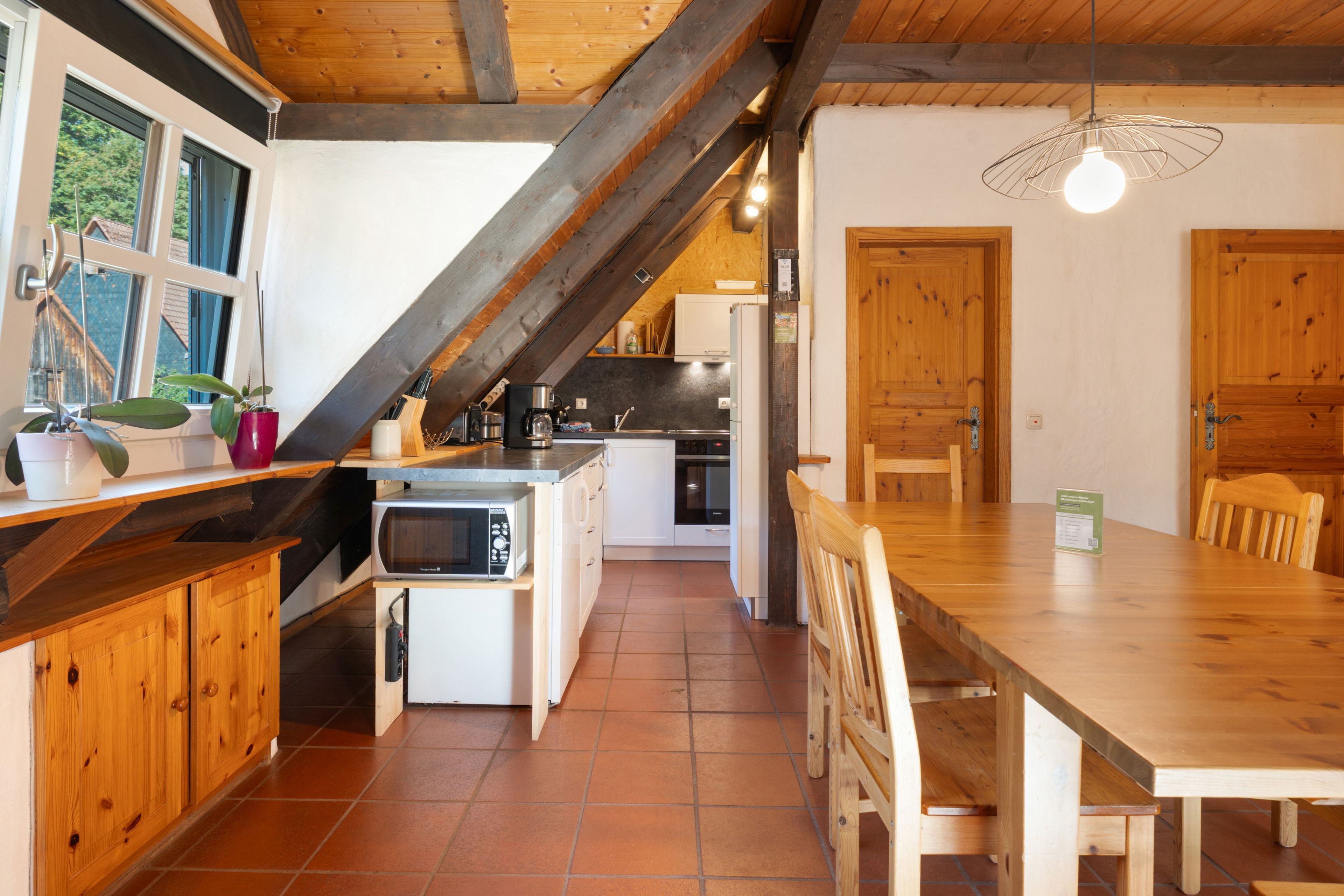 A kitchen with a wooden ceiling, a dining table, and a view of the outside.