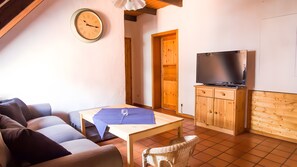 Una sala de estar con un sofá, una mesa, un televisor sobre un mueble de madera y un reloj en la pared.
