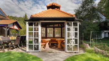 A gazebo with a tiled roof, open sides, and a central table with benches.