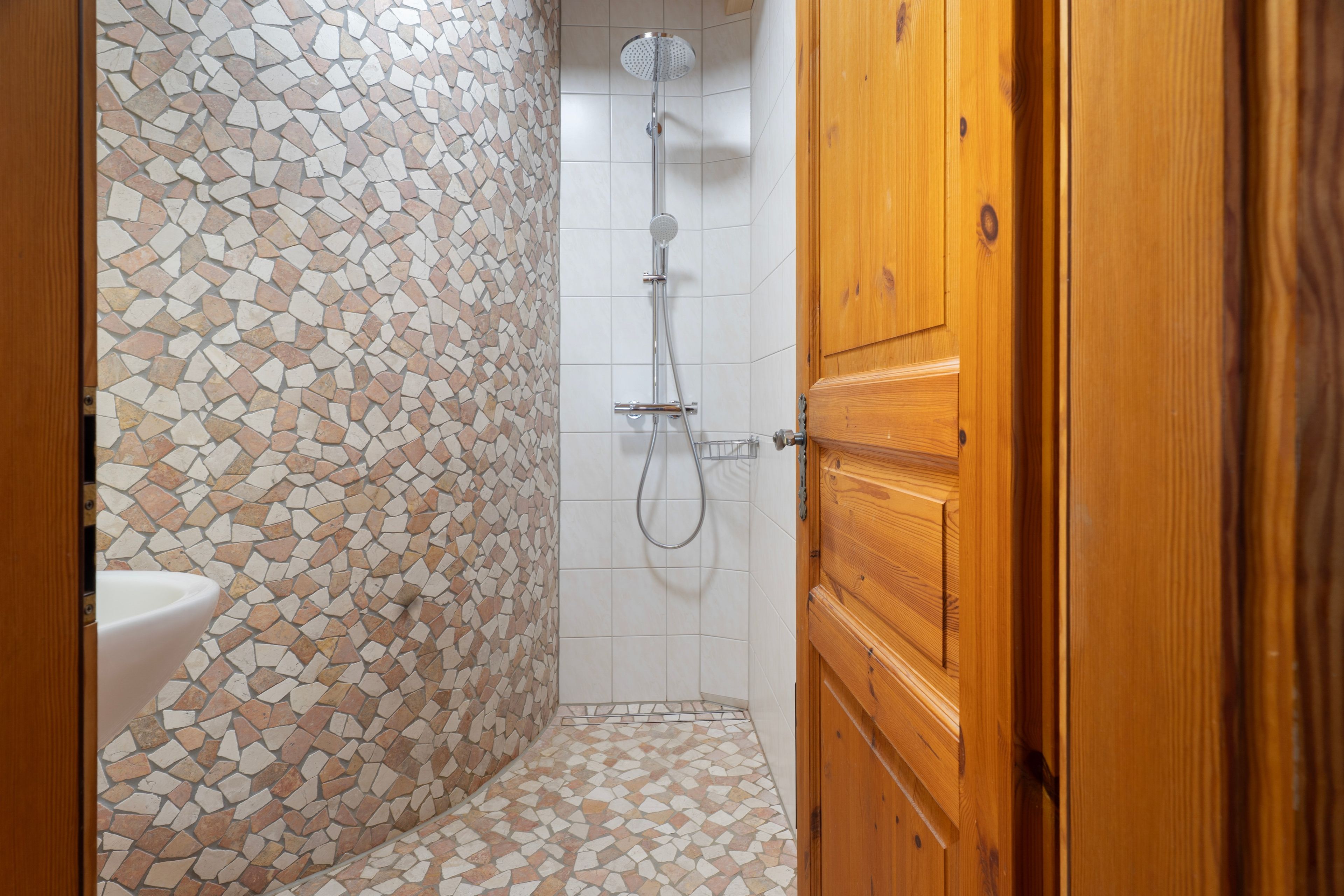 A bathroom with a mosaic tile wall, a shower, and a wooden door.