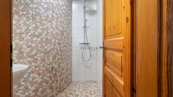 A bathroom with a mosaic tile wall, a shower, and a wooden door.