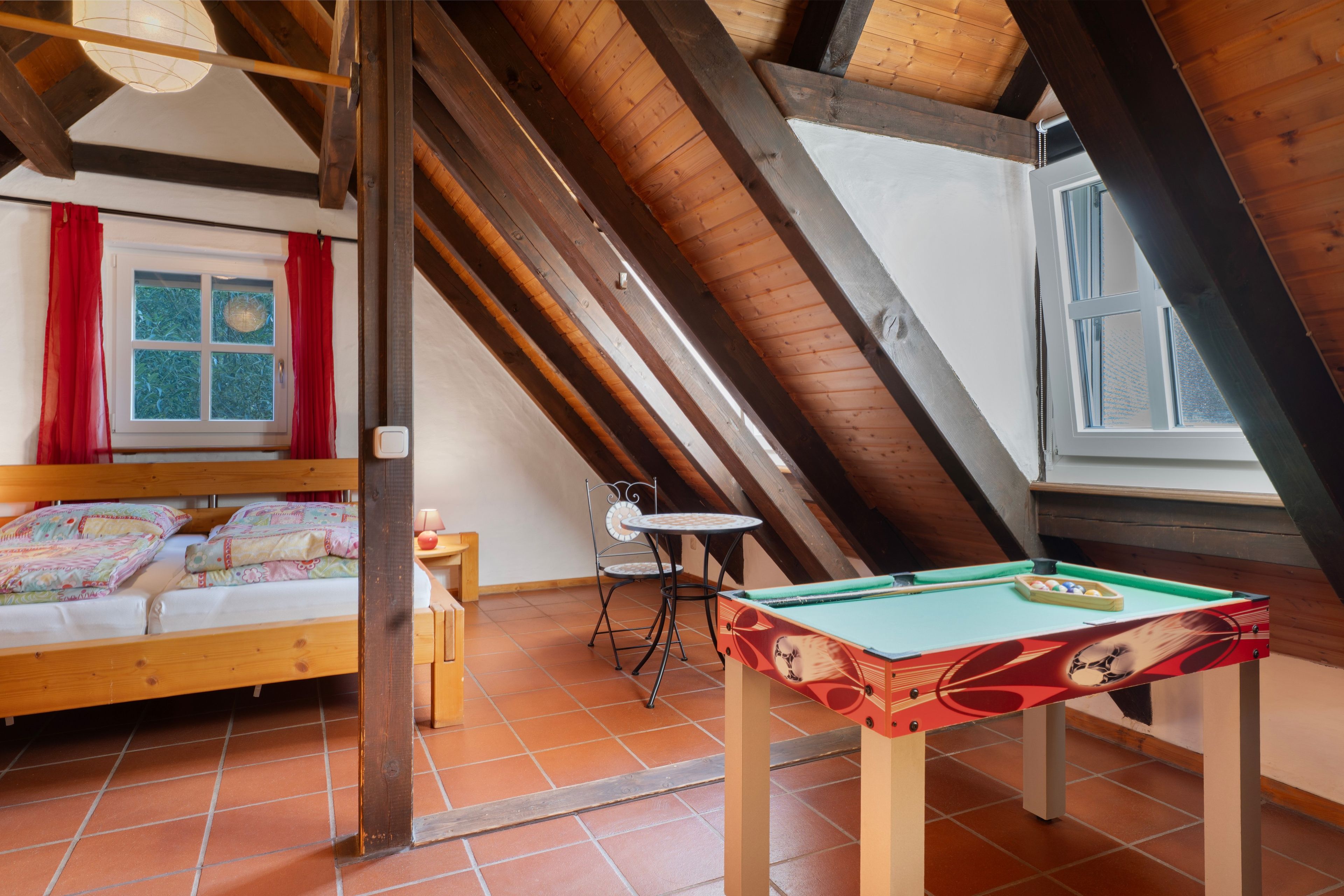 Een gezellige zolderkamer met een bed, een klein tafeltje en een pooltafel.