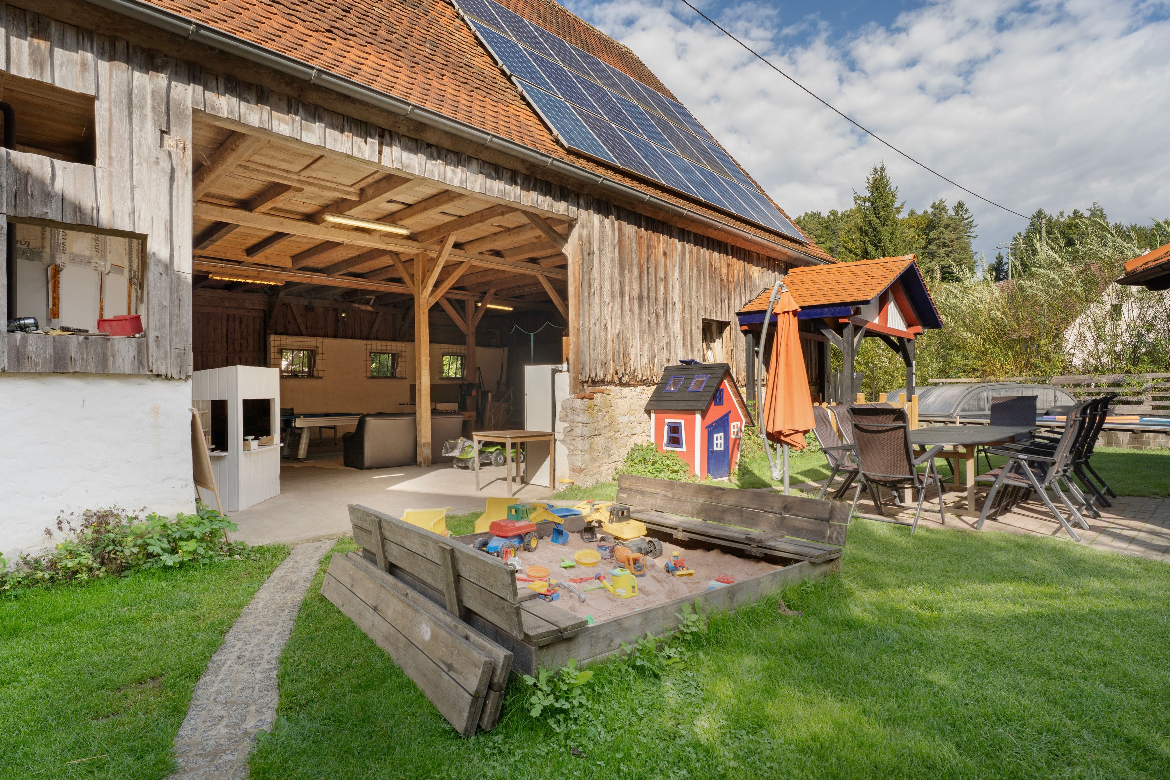 Ein rustikaler Schuppen mit überdachtem Außenbereich, Solaranlagen und einem Spielbereich mit Spielzeugfahrzeugen.