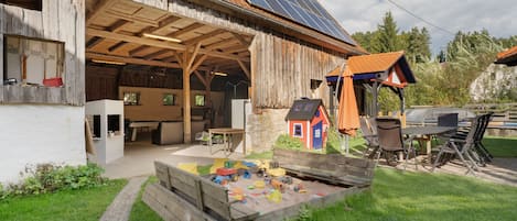 En rustik lade med et overdækket udendørs område, solpaneler og et legeområde med legetøj.'