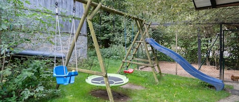 A wooden swing set with a slide, surrounded by greenery.