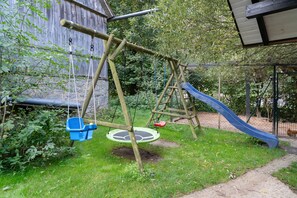 Un columpio de madera con un tobogán, rodeado de vegetación.