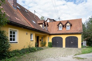 A yellow building with a tiled roof, two black doors, and a cobblestone path leading to the entrance. - Drei Zinnen Holiday Apartment (Hiltpoltstein)