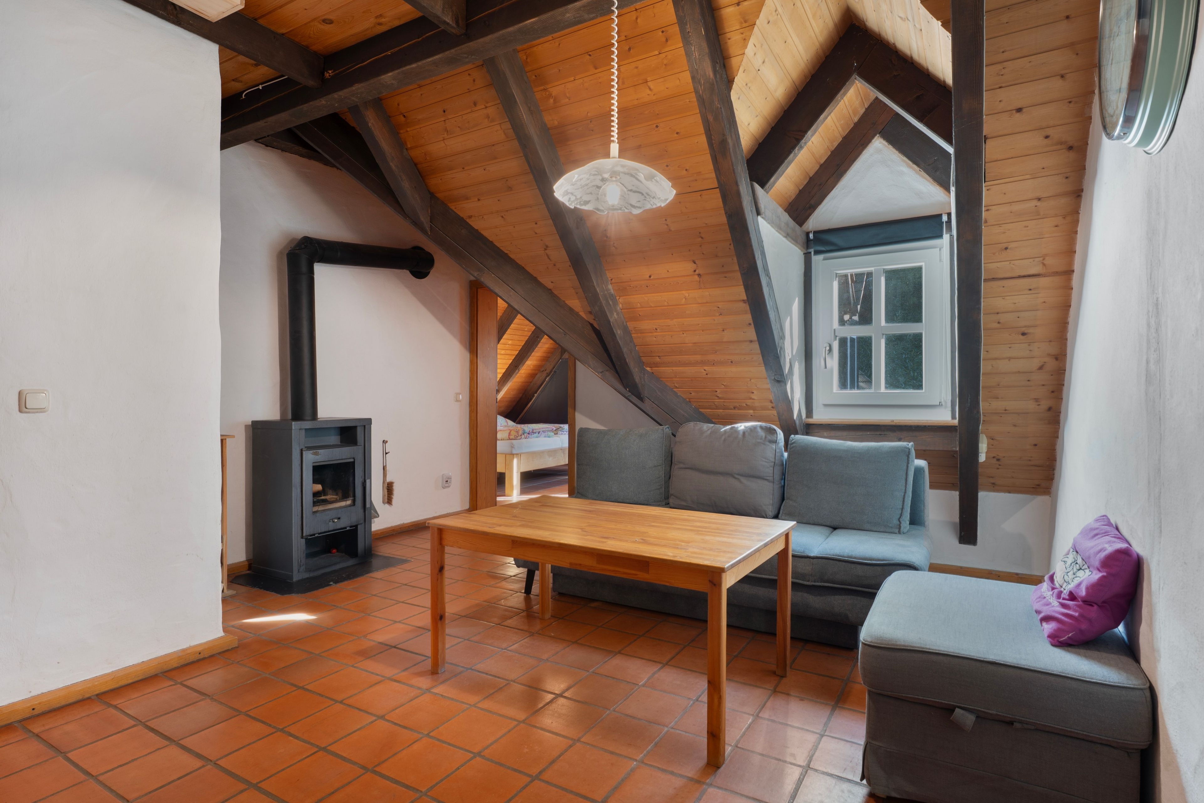 Ein gemütliches Dachzimmer mit Holzboden, einem fest eingebauten Holzofen, einer Couch und einem Esstisch.