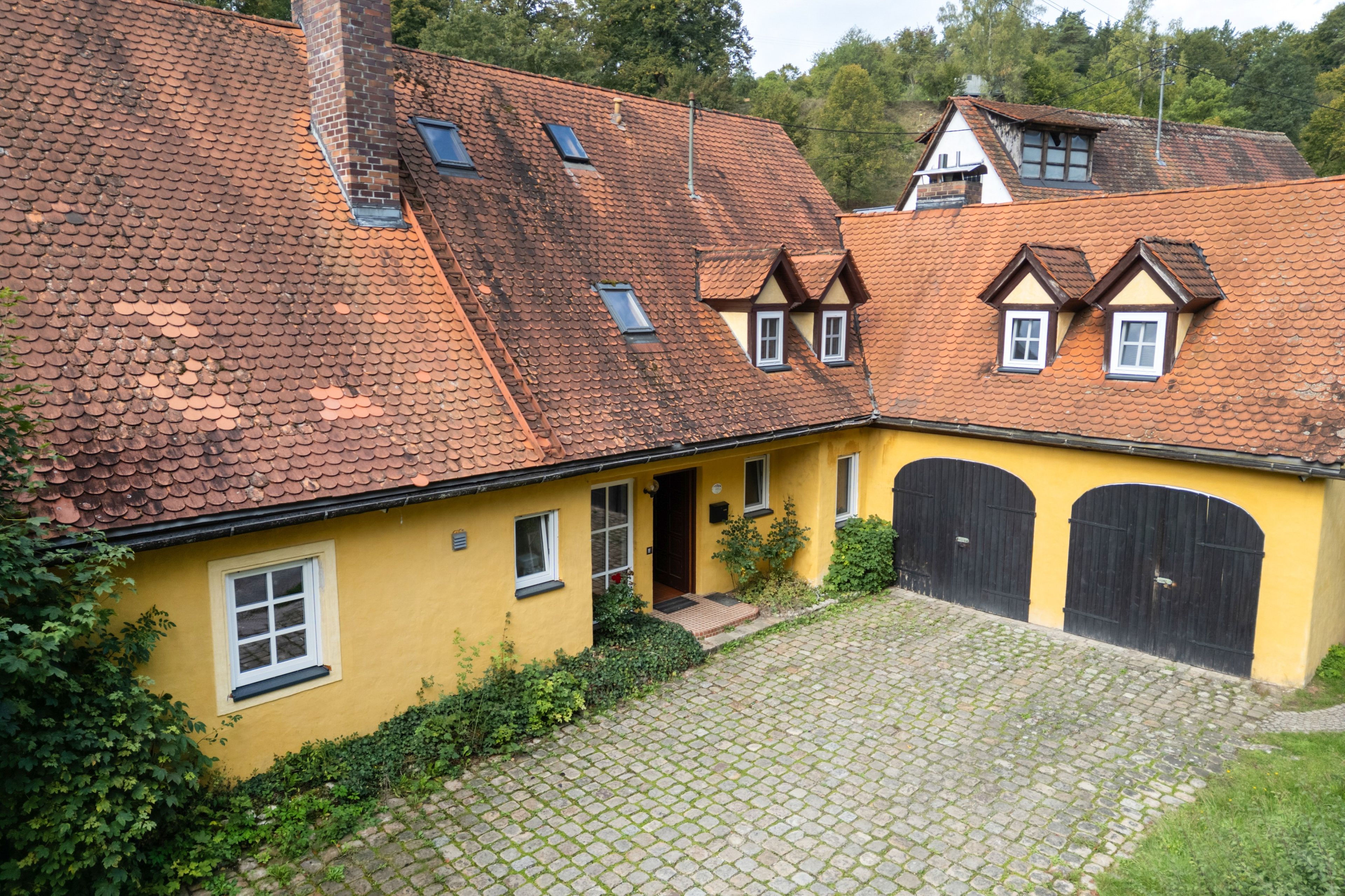 Ein gelbes Gebäude mit einem Ziegeldach, einem Innenhof und einem schwarzen Tor.