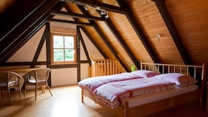 Un dormitorio con techo inclinado, una cama con almohadas, una silla y un ventanal.