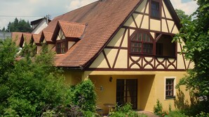 Una casa tradicional de entramado de madera con techo inclinado, un pequeño jardín y una puerta visible.