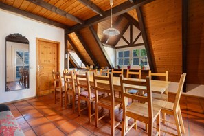 Un comedor con mesas y sillas de madera, una cocina al fondo y un techo inclinado con vigas de madera.