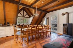 Een ruime keuken met een hoge plafond, houten balken, een eettafel met stoelen, een inbouwoven en uitzicht door het raam.
