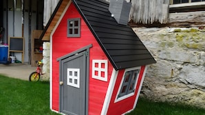 Una casa pequeña de color rojo y gris con techo negro, una puerta y ventanas.