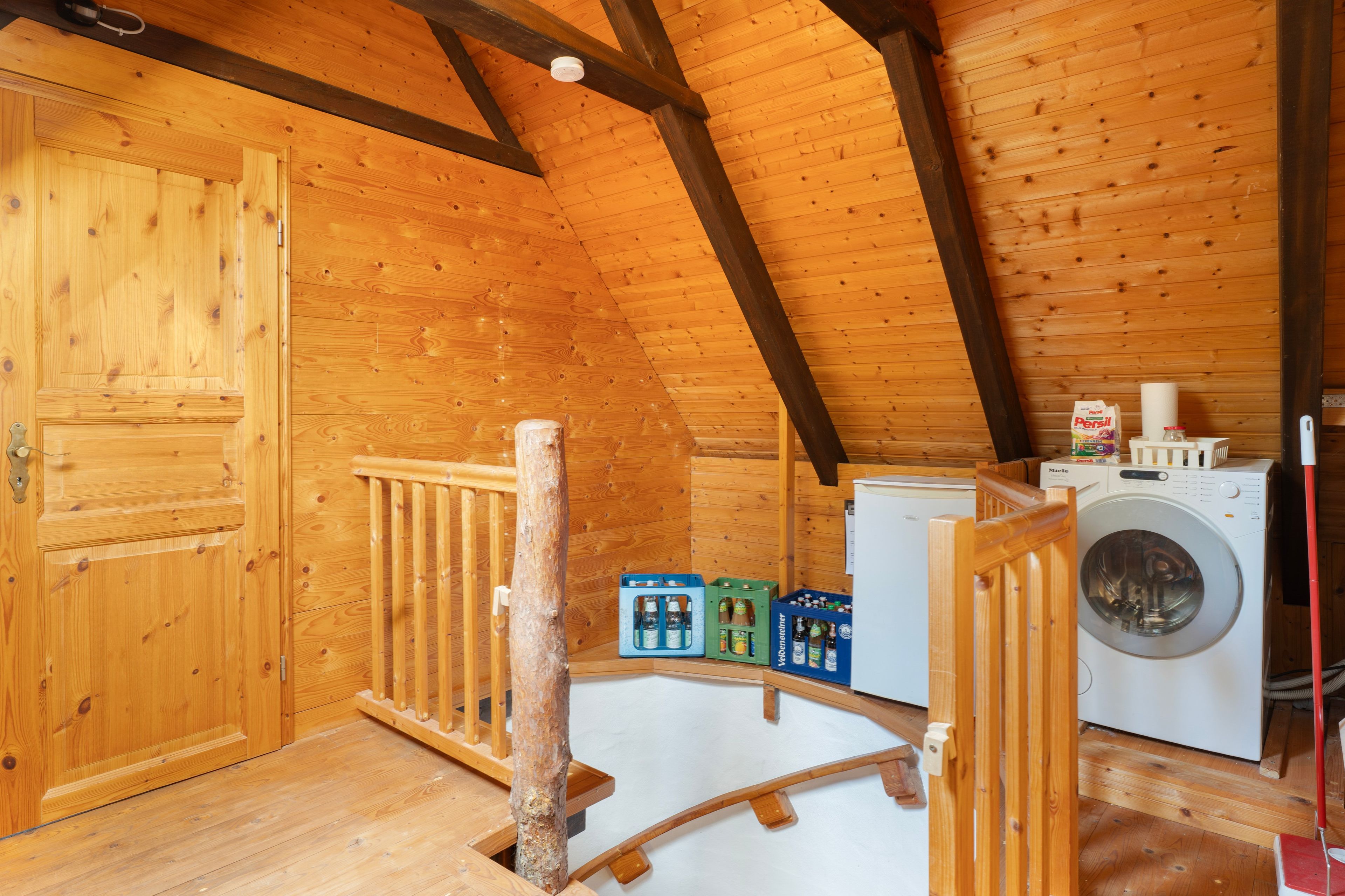 A wooden interior with a washing machine, a drying rack, and a door.