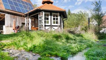 Een landelijke woning met een zonnepaneelinstallatie op het dak, een kleine tuin en een smalle beek.
