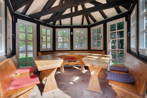 Un espace de repos abrité, doté de bancs et de tables en bois, de grandes fenêtres et offrant une vue sur la verdure environnante.
