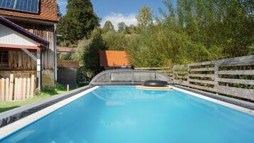 A swimming pool with a slide, surrounded by a wooden fence and trees.