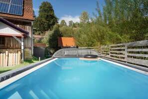 Una piscina con tobogán, rodeada por una valla de madera y árboles.