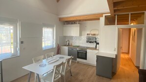 A spacious kitchen with wooden beams, white cabinetry, and a dining area with a table and chairs.