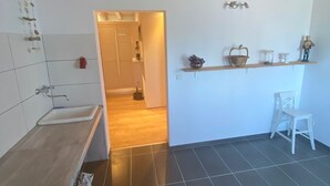 A modern kitchen with a wooden ceiling, a sink, a chair, and a shelf with various items.