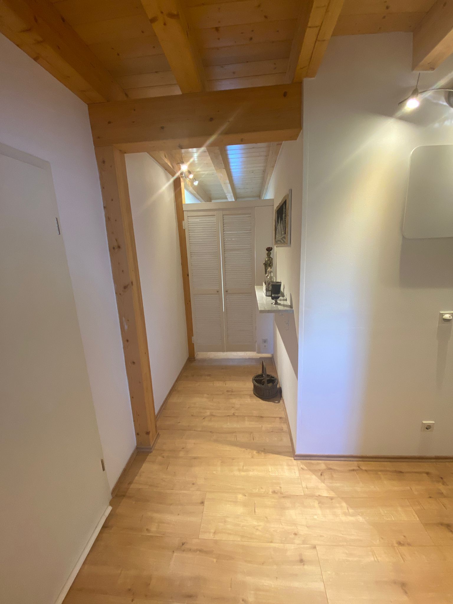 Ein schmaler Flur mit Holzboden, einer weißen Tür und einem Kleiderschrank mit Schiebetüren.