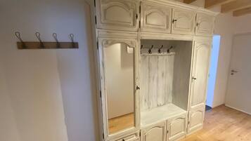 Ein großer, weißer Kleiderschrank mit mehreren Türen und Schubladen, ein Holzregal mit Haken sowie ein Holzboden.