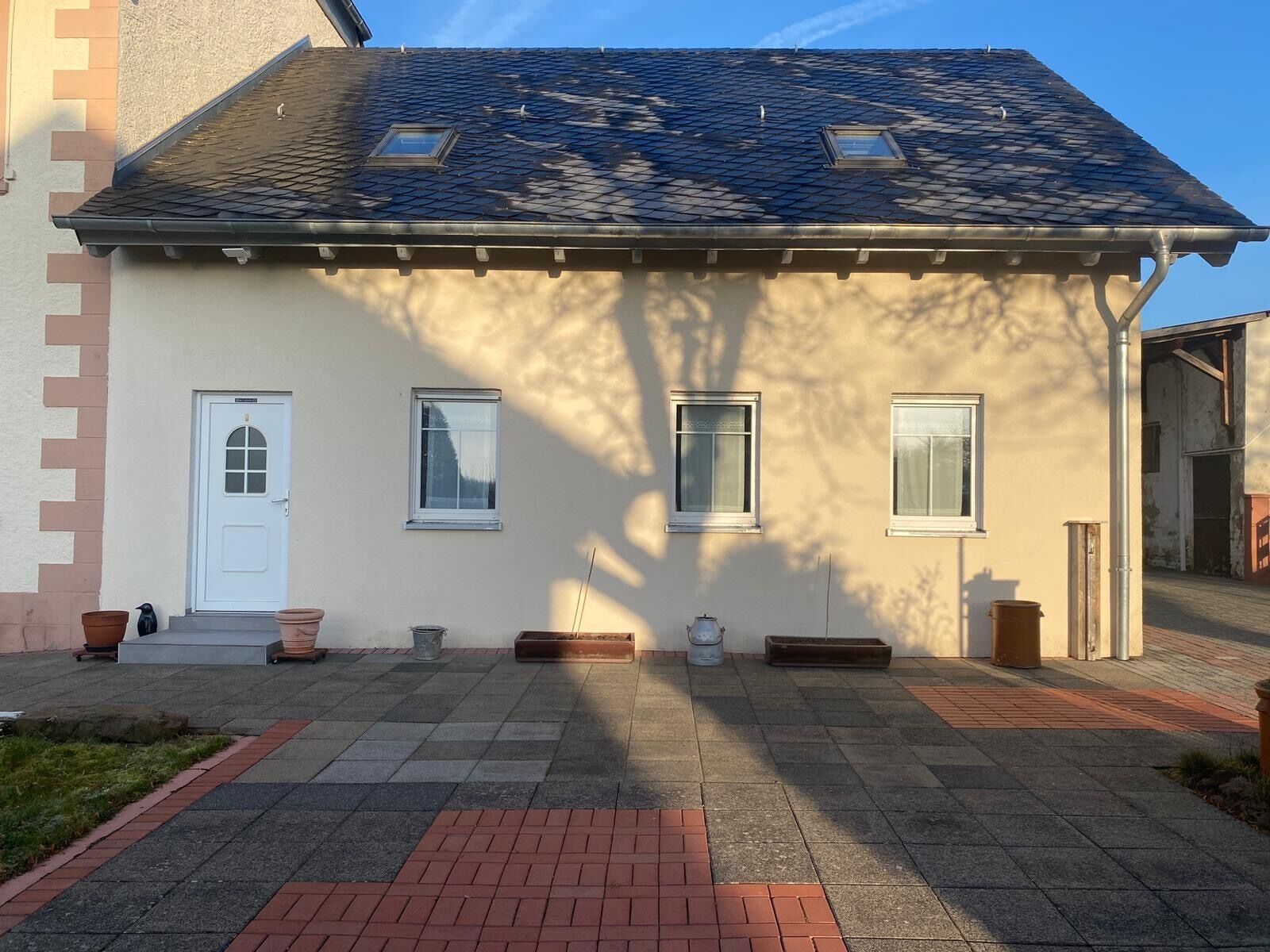 Un bâtiment doté d’un toit en pente, d’une porte blanche et de trois fenêtres.