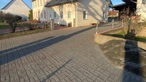 A large building with a sloped roof, a paved driveway, and a fenced courtyard.