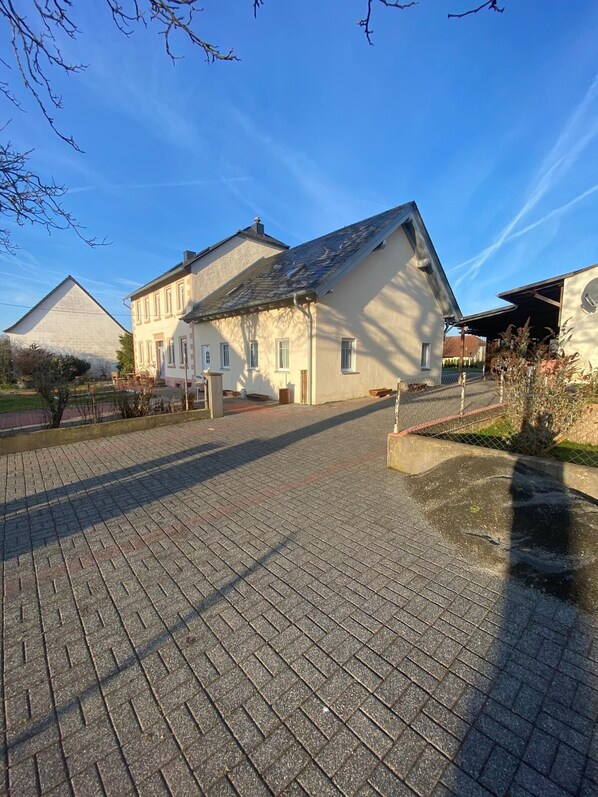 A large building with a sloped roof, a paved driveway, and a fenced courtyard.