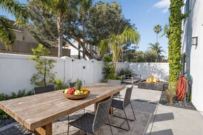 An outdoor patio with a wooden table, chairs, a fruit bowl, and a fire pit.