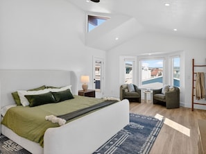 A bedroom with a large bed, a sofa, a chair, a small table, and a view of buildings through a window. - Outrigger Beach Retreat w/ Private Path & Firepit (Oxnard)