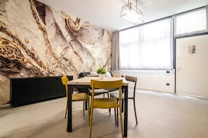 A modern dining area with a marble wall, a round table, and yellow chairs.