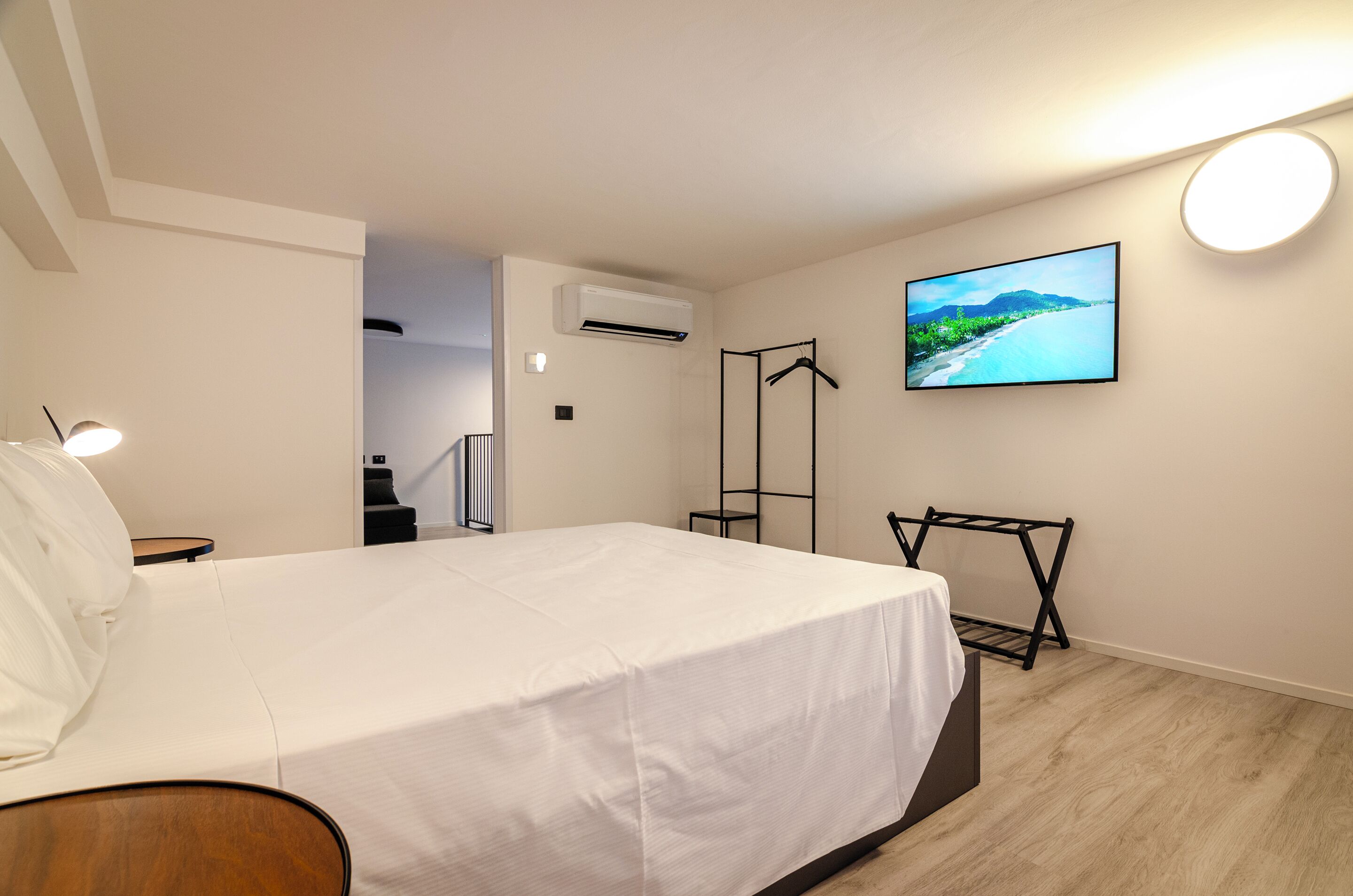 A hotel room with a bed, a TV mounted on the wall, an air conditioning unit, and a wooden floor.