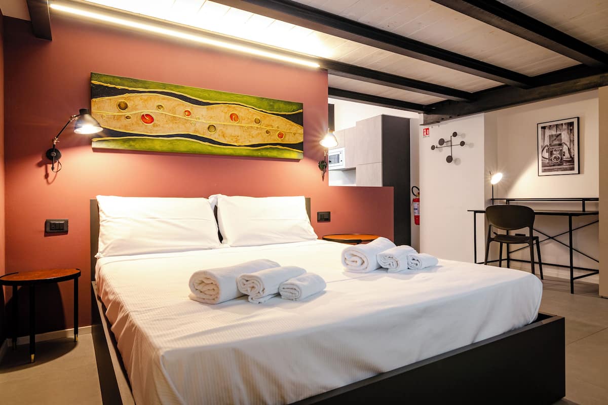 A hotel room with a bed, a desk, a chair, and a wall-mounted artwork.