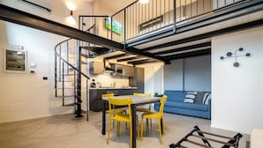 A modern interior with a dining area, kitchen, and living space, featuring a staircase and a blue sofa. - Saffi Lofts (Bologna)