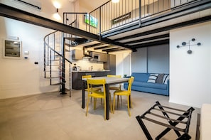 A modern interior with a dining area, kitchen, and living space, featuring a staircase and a blue sofa.