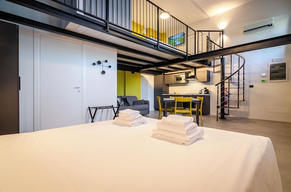 A modern apartment with a bed, a dining area, a kitchen, and a staircase.