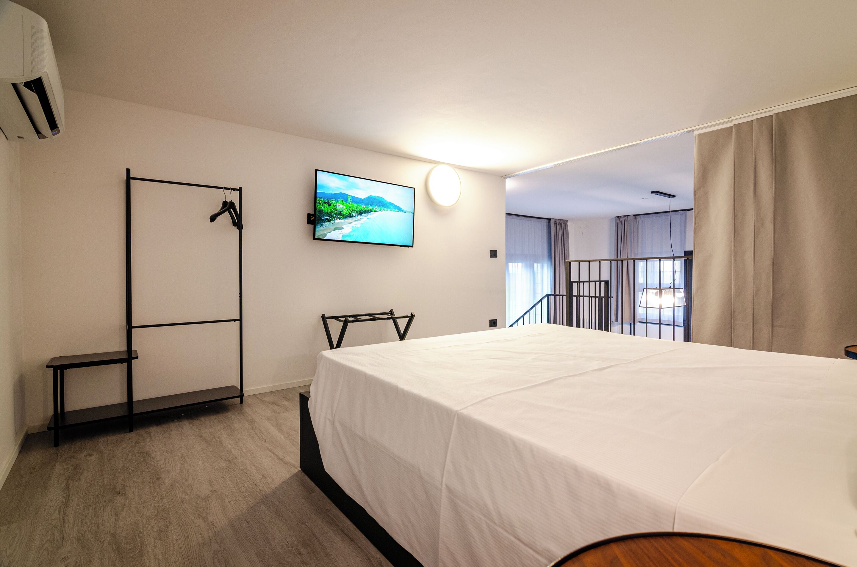 Une chambre d’hôtel avec un lit, un téléviseur fixé au mur, un porte-manteau et une porte.