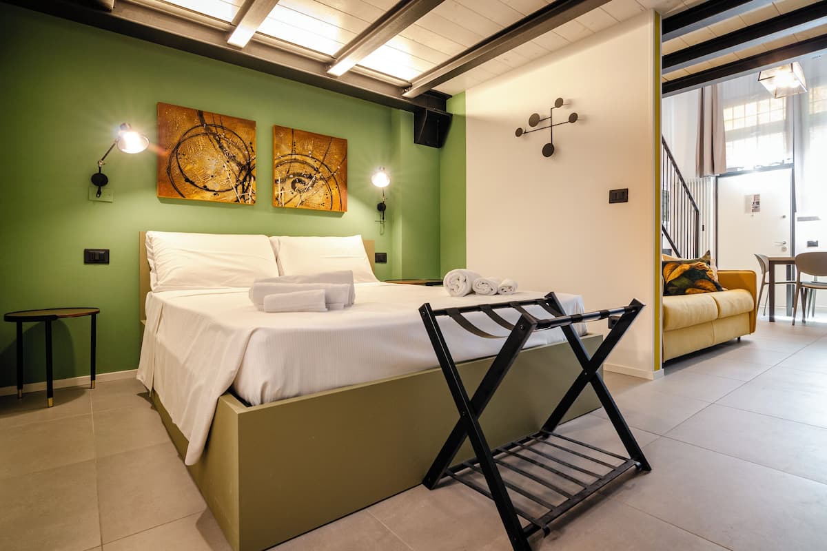 A bedroom with a bed, two wall-mounted lamps, a painting, a small table, and a chair.