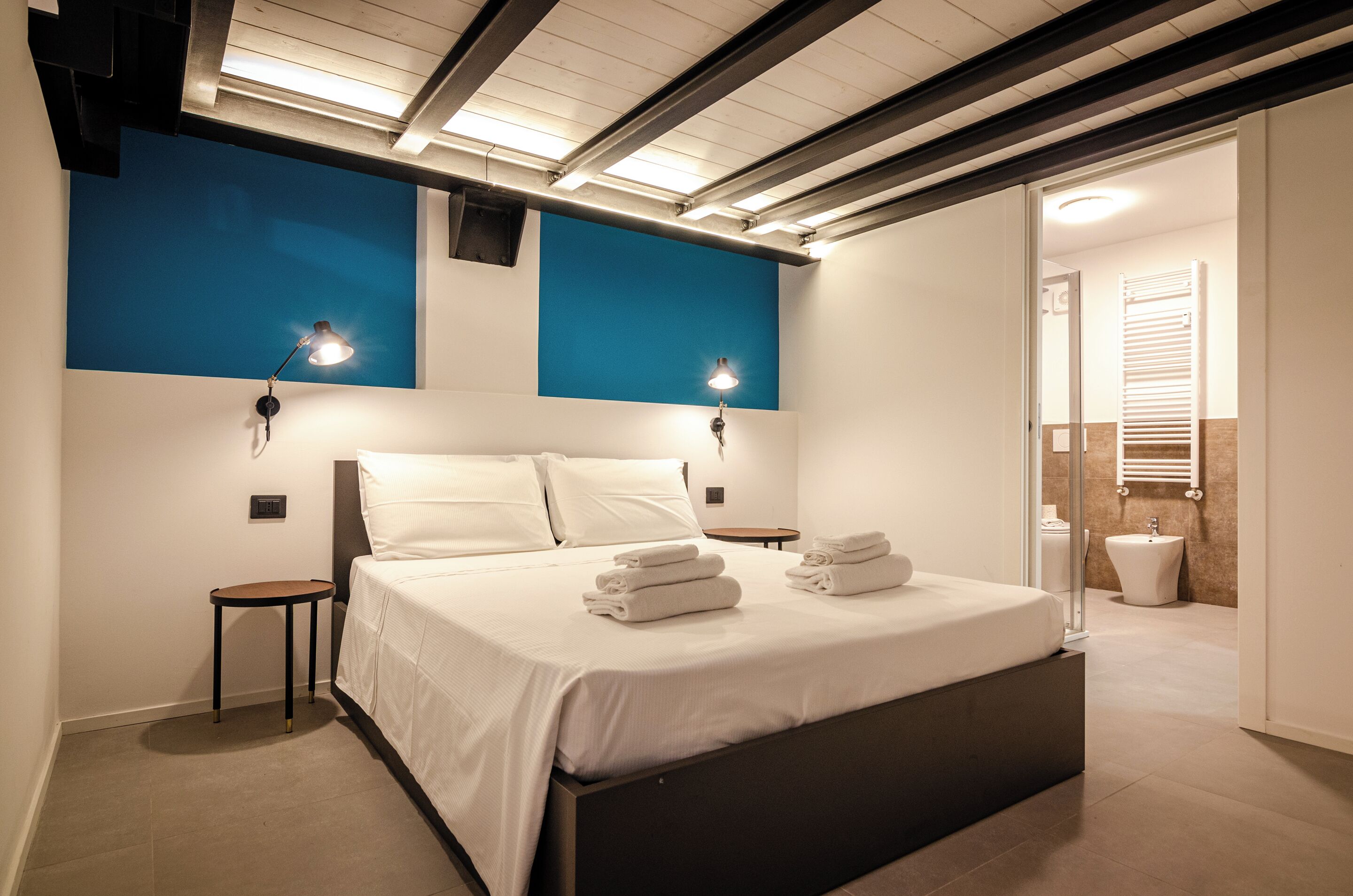 A modern bedroom with a bed, bedside tables, and a bathroom visible through an open door.