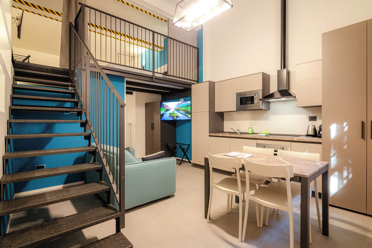 A modern kitchen with a dining area, a staircase, and a flat-screen TV.