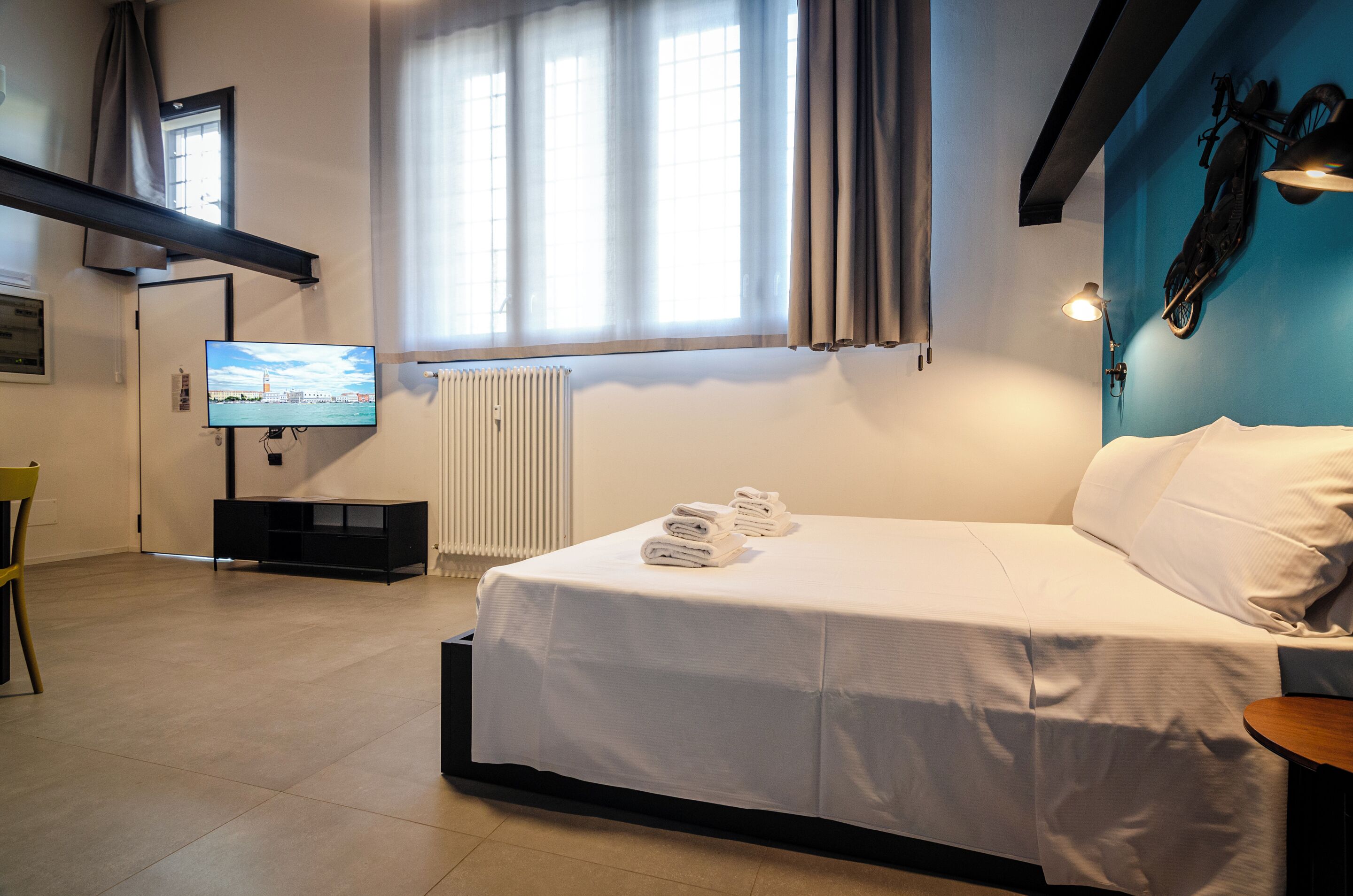 Een hotelkamer met een bed, een televisie, een radiator en een raam met gordijnen.