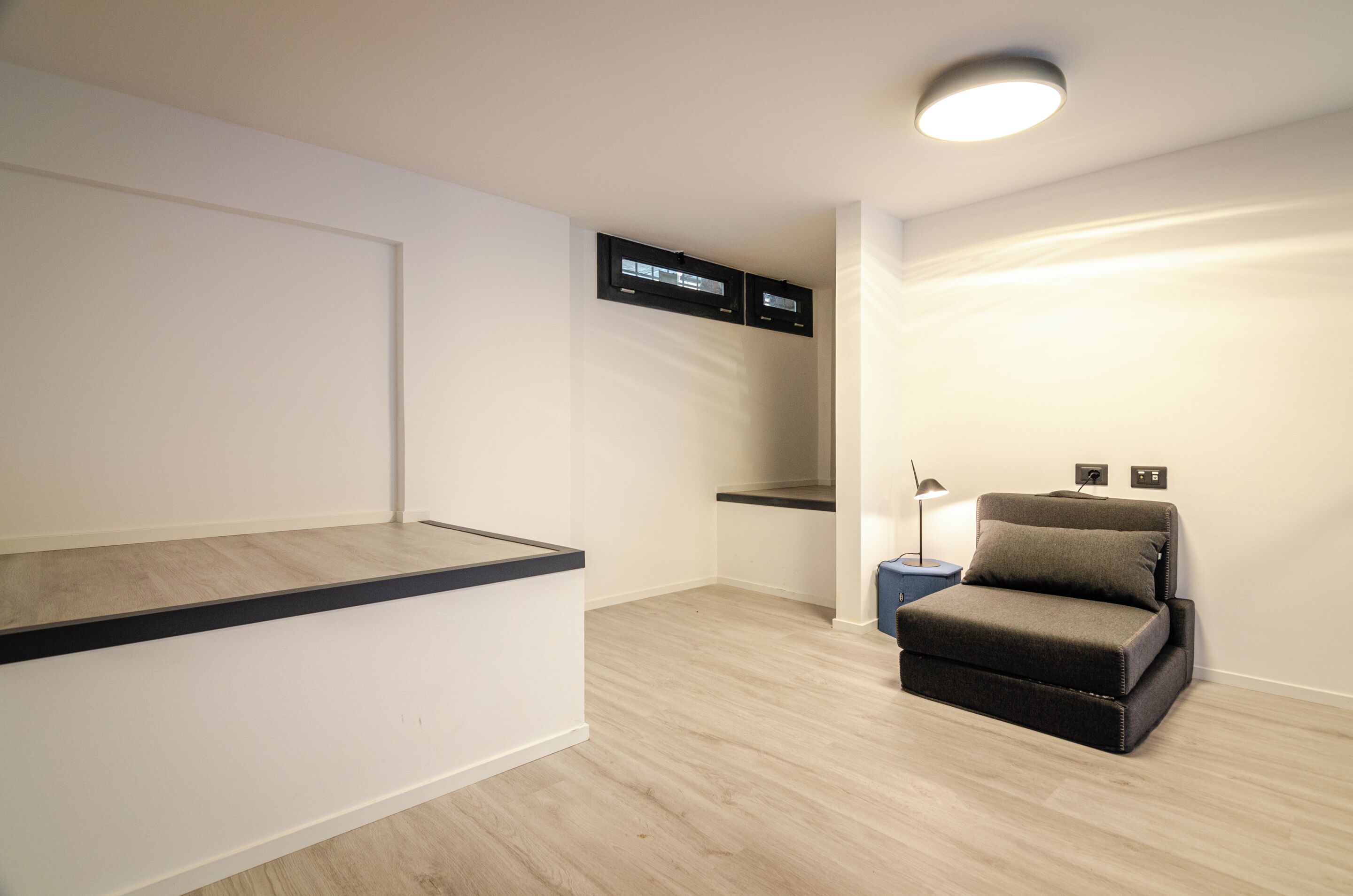 A modern room with a built-in bench, a small sofa, a desk, and a ceiling light fixture.