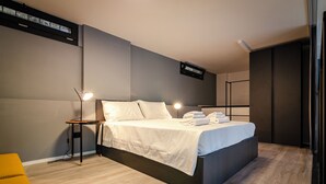 A modern hotel room with a large bed, bedside tables, a desk, and a built-in TV. - Saffi Lofts (Bologna)
