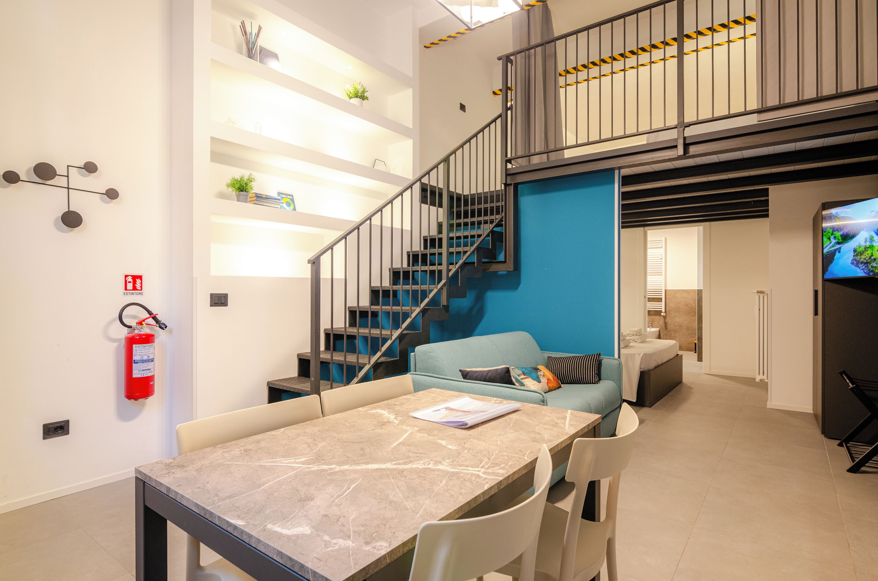 A modern interior with a dining area, blue accent wall, staircase, and a flat-screen TV.