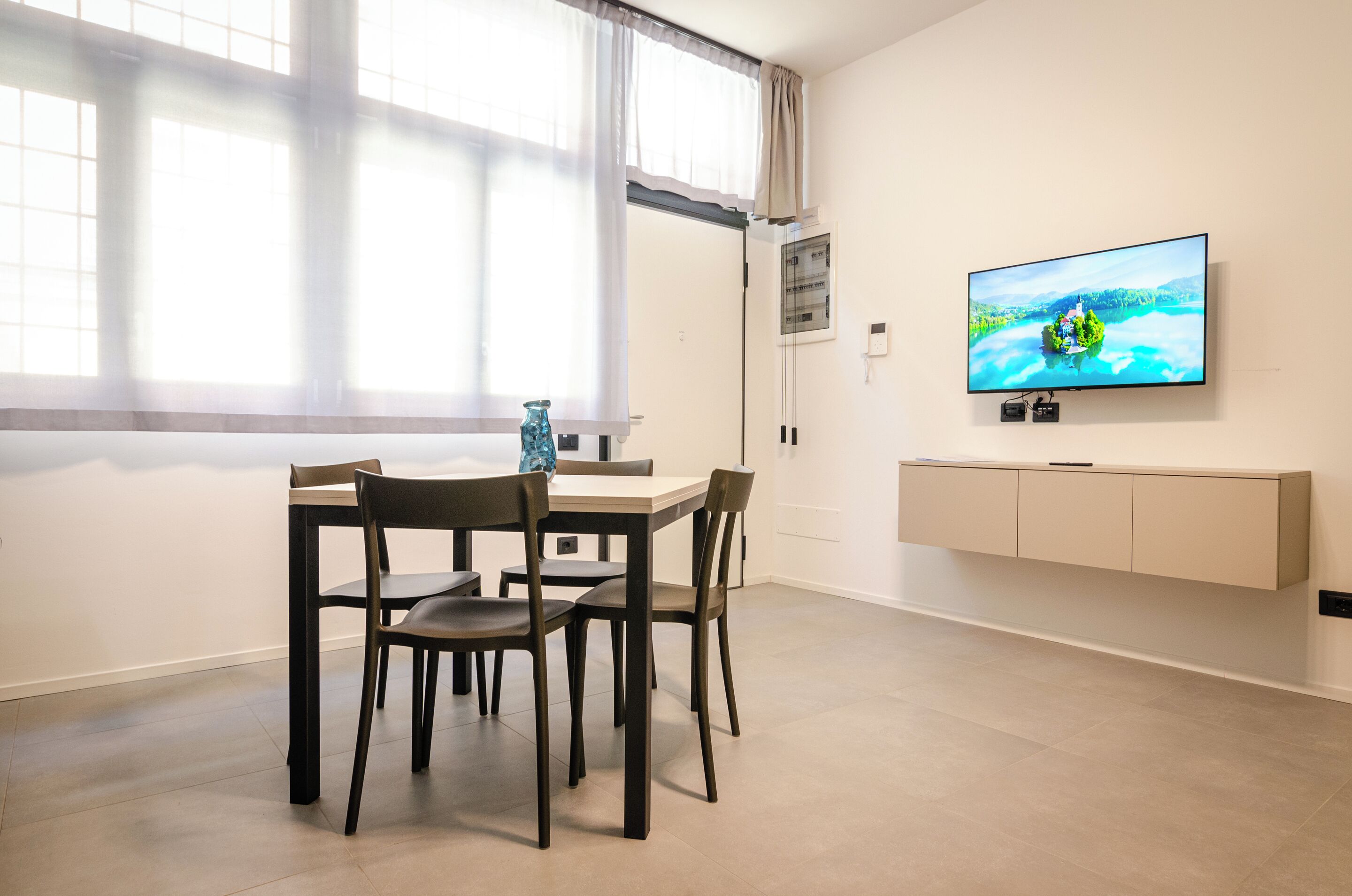 A modern dining area with a table and chairs, a television on the wall, and a window with curtains.